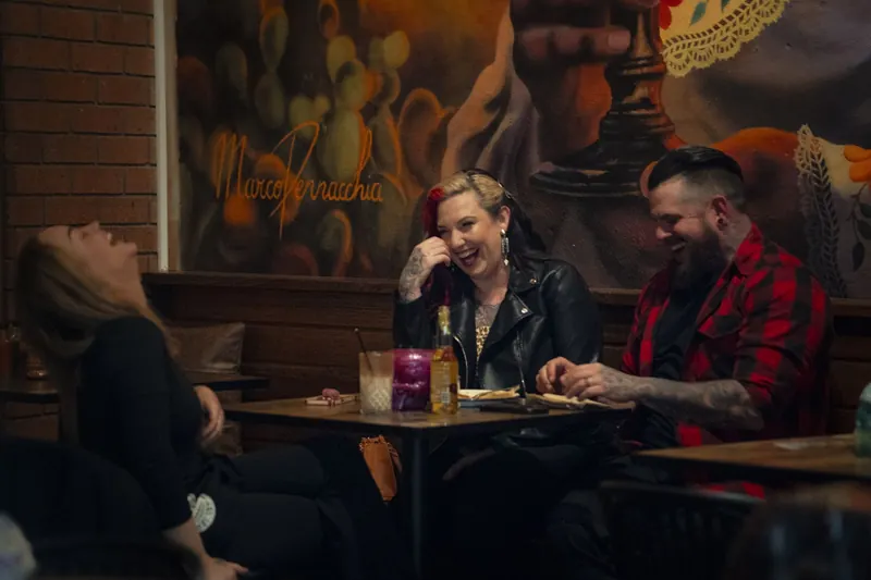 Guests laughing over dinner beneath the Catrina mural